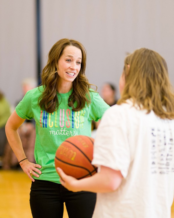 Abby Cox speaks with a unified sports athlete on a basketball court.
