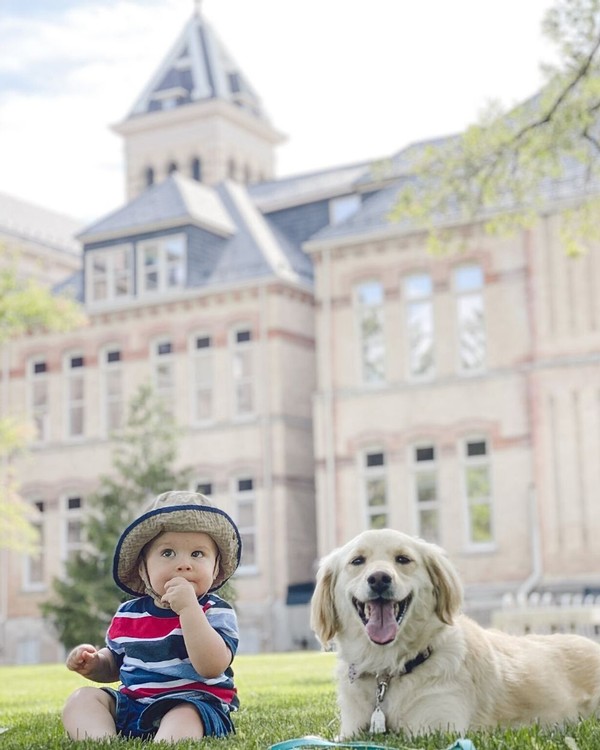 A baby and dog relax in the grass in front of Old Main.