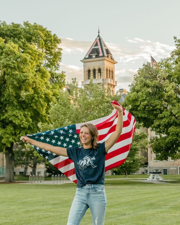 A female USU student holds a U.S. flag above her head in front of Old Main
