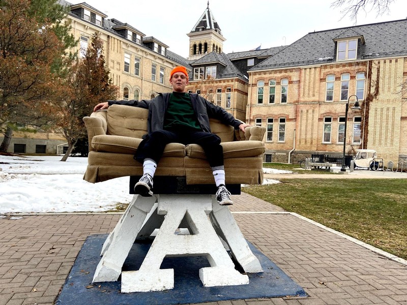 A male USU student sits on a loveseat atop the Block A at Old Main