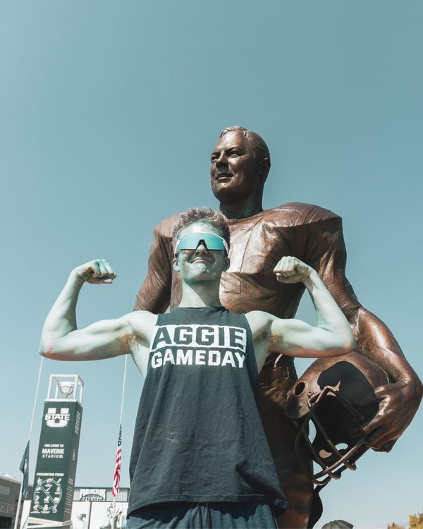 A USU student, covered in blue body paint, flexes in front of the Merlin Olsen statue.