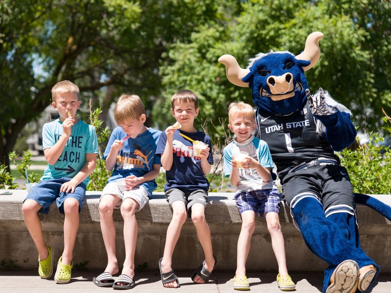 Big Blue sits on a bench with four young boys, while eating ice cream