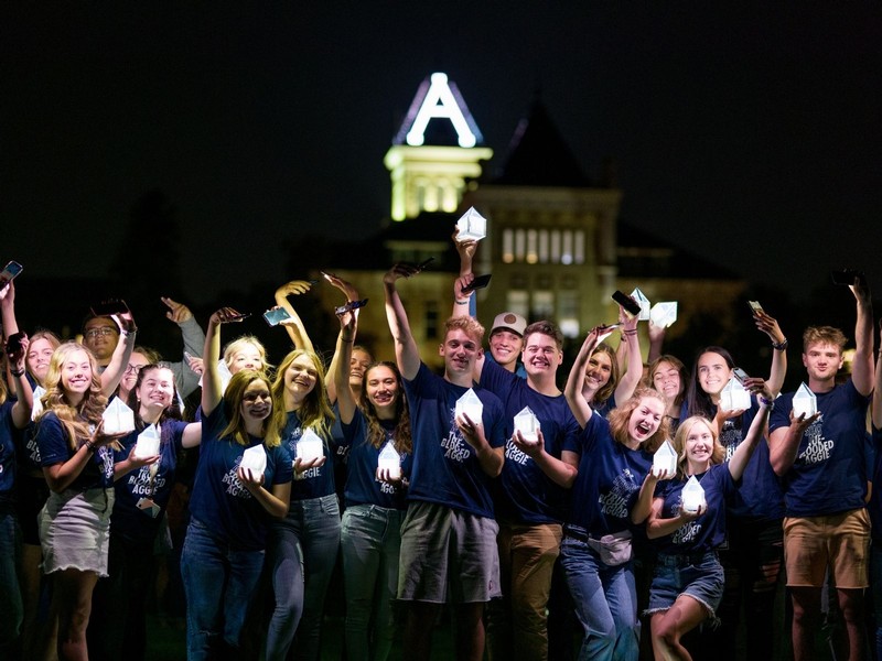 New USU students pose for a photo in front of Old Main at night.