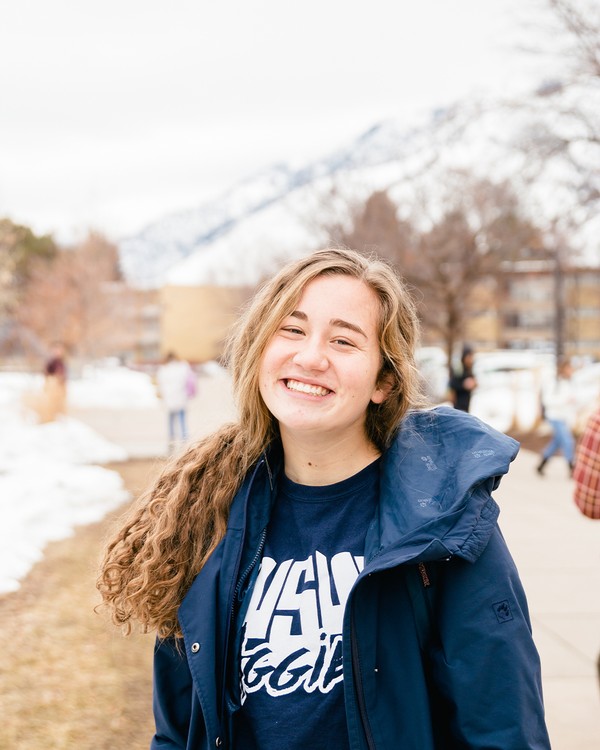 Student wearing Utah State jacket on campus during winter.