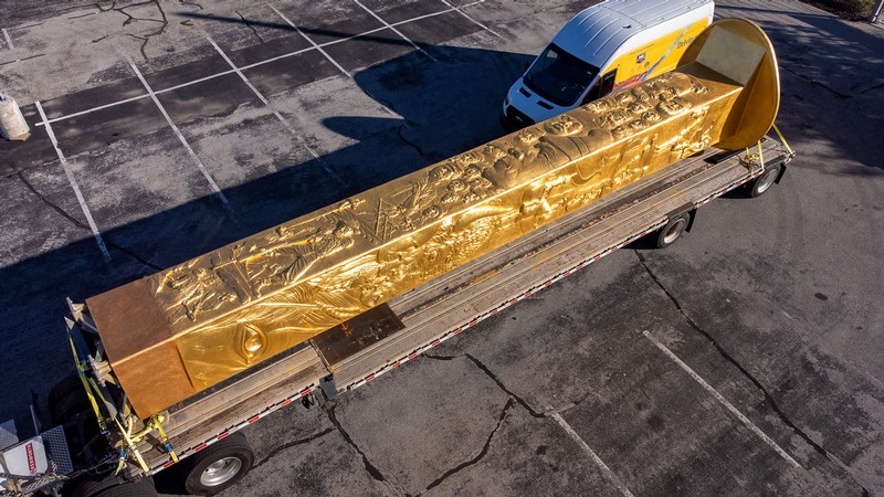 A giant golden spike on a flatbed trailer parked in a parking lot.