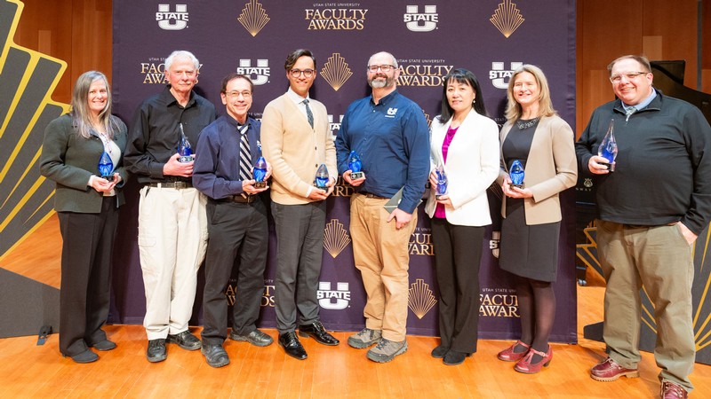 Faculty members hold awards at a ceremony.