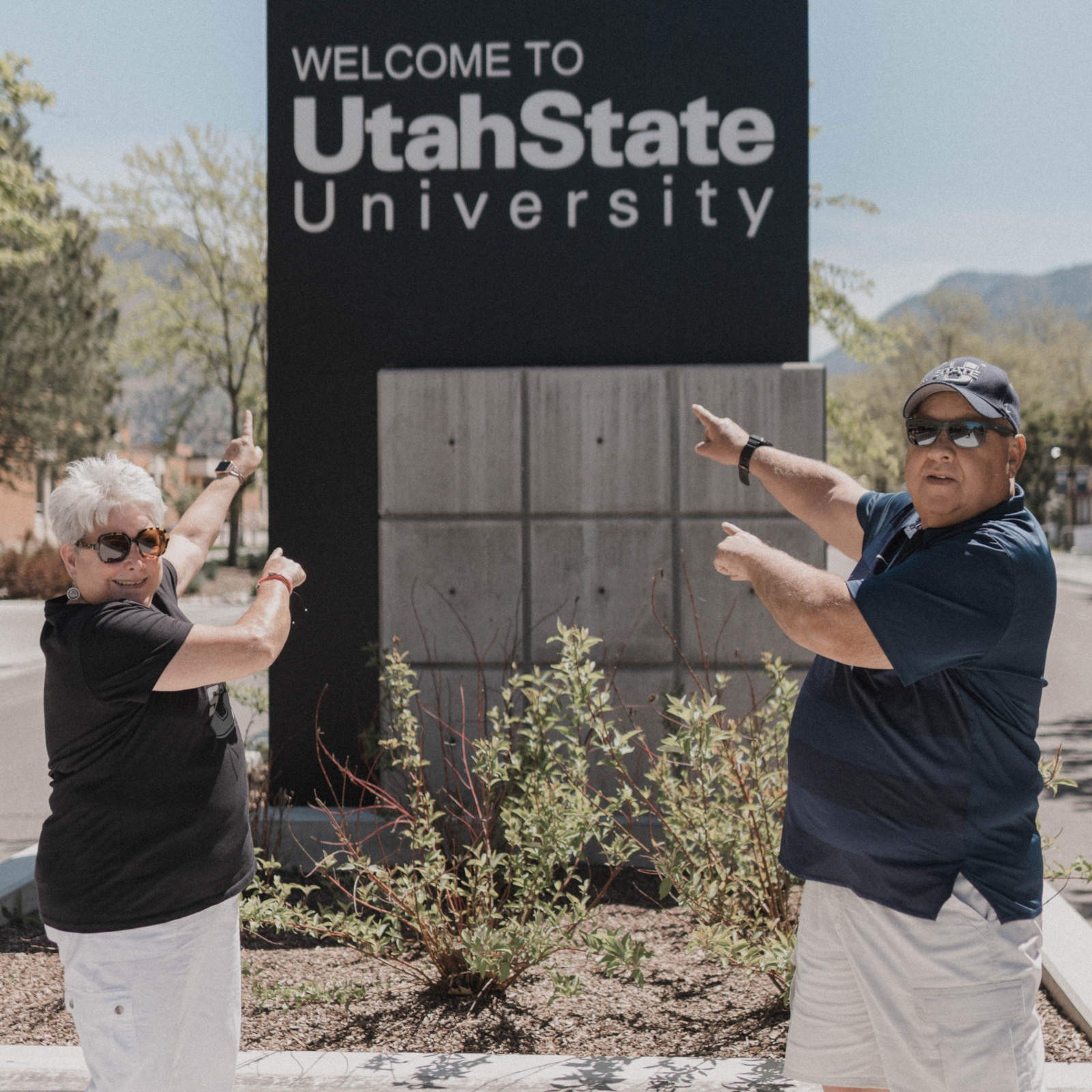 Two people pointing at the Welcome to USU sign.