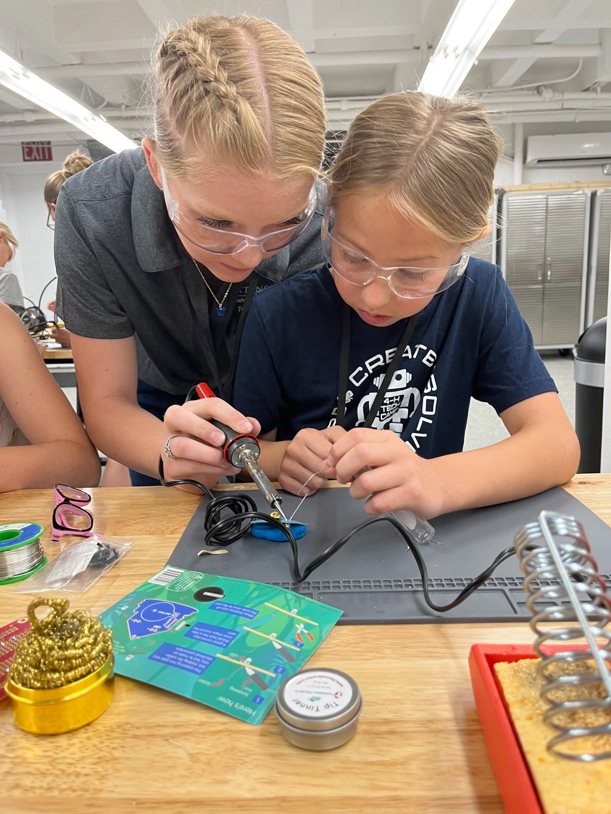 Two girls solder a project in a lab classroom.