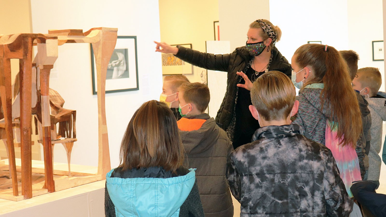 A woman shows fourth-graders abstract wooden sculptures during a USU art museum tour.
